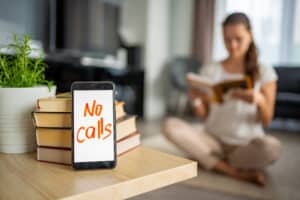 Digital detox concept photo. Smartphone with text No Calls and woman reading book in background