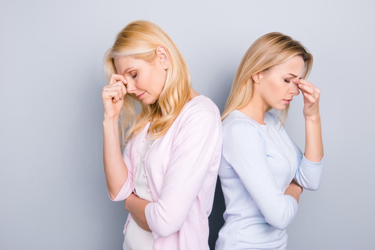 Sad tired unhappy disappointed parent and adult child standing back to back holding fingers hands between eyes on nose keeping eyes closed having negative emotions isolated on grey background